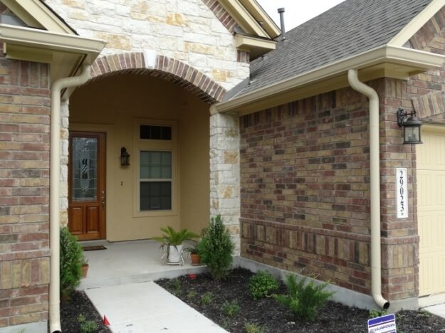 two downspouts by the front porch of a stone and brick home