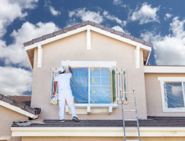 What to Look for in a House Painter Professional house painter has the shutters and trimming covered as he paints the exterior of a home.