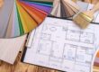 Home floor plan, paint samples, and paint brushes fanned out on a hardwood floor depict the design plan for house painting.
